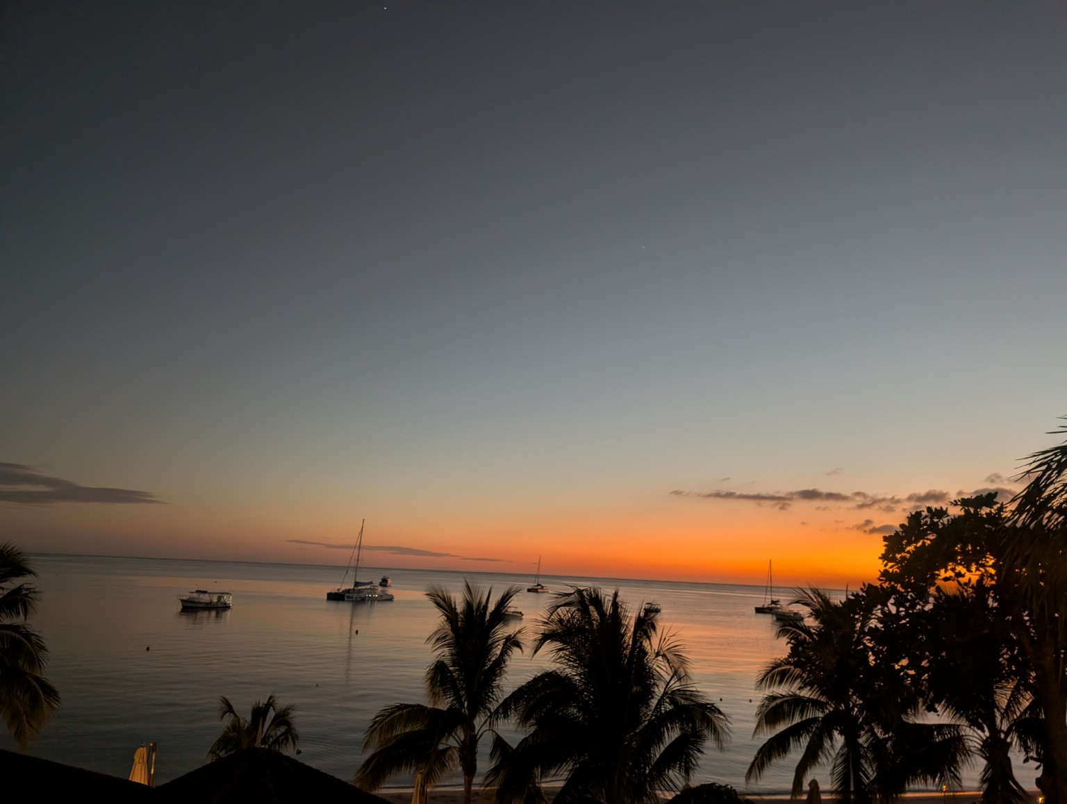 Orange sunset over calm tropical water and sailboats